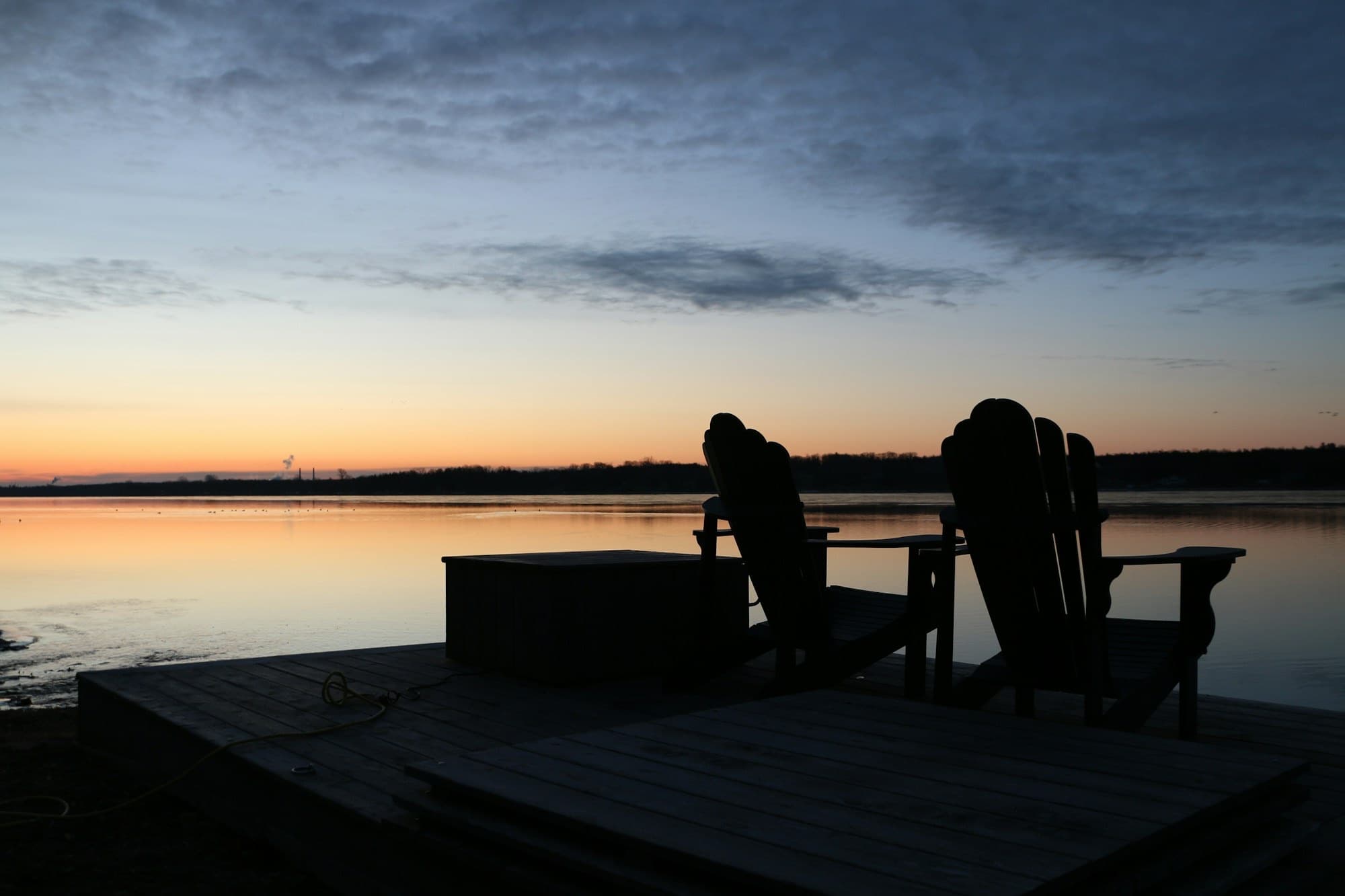 Adirondack chairs on a waterfront deck at sunset